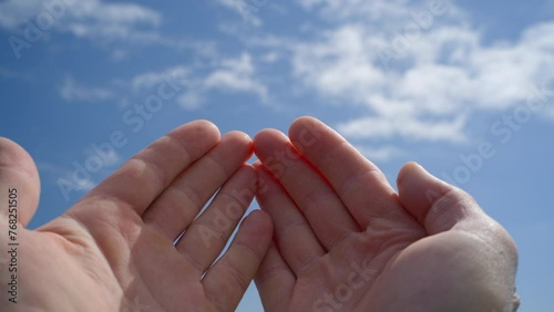 Hands, palms raised, in prayer and supplication, stretch out to the clear blue sky.