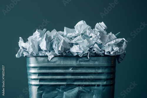 A metal trash can is filled with paper