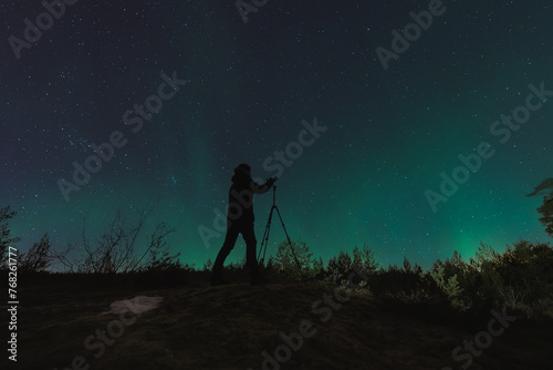 A landscape astro photographer with a camera on a tripod takes pictures of the starry sky and the northern lights.