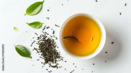 A cup of green tea on the right, loose green tea leaves on the left, with tea leaves scattered around, and one leaf floating on the teas surface. Well-lit image, vibrant colors.