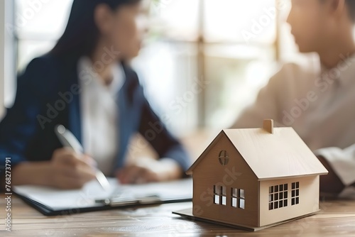 Real estate agent and client discussing house loan terms with model house on table in blurred background. Concept Real Estate Negotiation, House Loan Terms, Model House, Client Meeting photo