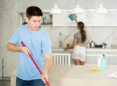 Guy mops floor until it shines during group cleaning in kitchen