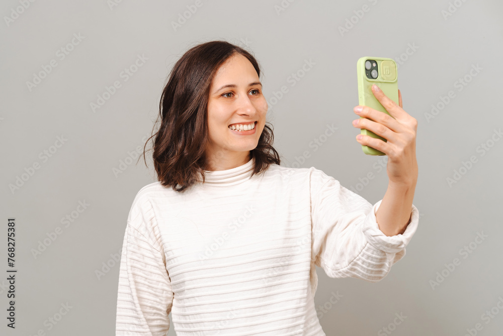 Studio portrait of a wide smiling woman taking a selfie shot with her phone over grey background. Studio portrait of a wide smiling woman taking a selfie shot with her phone over grey background.