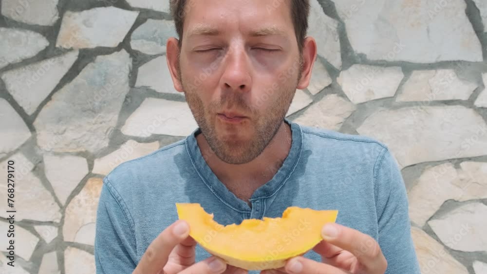 Happy Caucasian young man eating slice of fresh ripe melon cantaloupe in hot summer day outdoors. Healthy diet food on vacations. Handsome guy eats refreshing tasty fruit Happy Caucasian young man eating slice of fresh ripe melon cantaloupe in hot summer day outdoors. Healthy diet food on vacations. Handsome guy eats refreshing tasty fruit