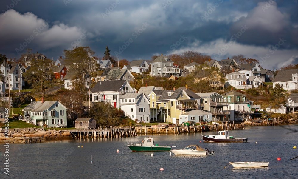 Lobster boats anchored in Stonington bay, Maine, with New England style houses on the shore in the background.