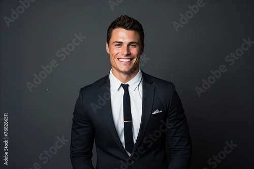 Portrait of a happy young man in black suit on grey background