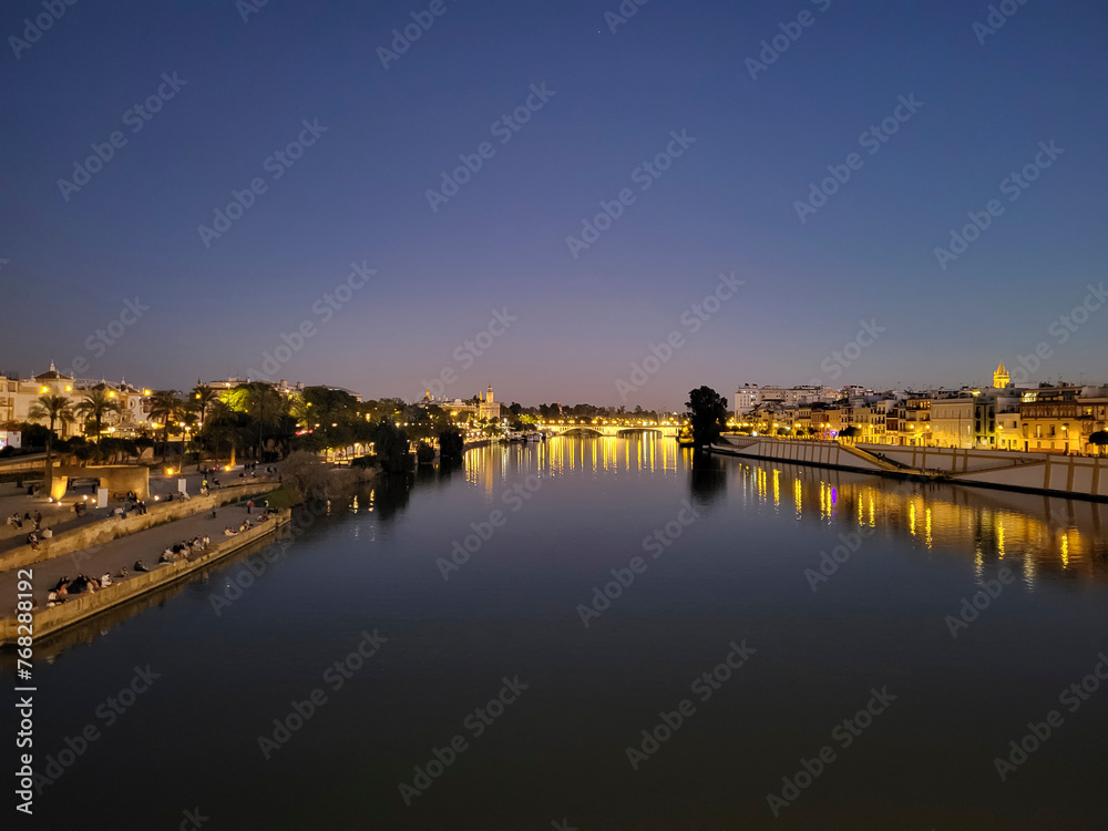 View of the Guadalquivir River in the night illuminations at sunset in Seville, Andalusia, Spain