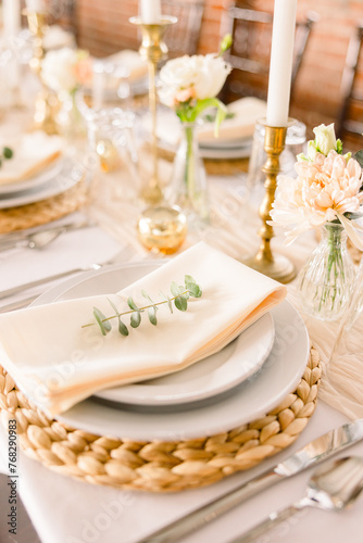 A close-up of a dinner plates with napkins, silverware, candles, and florals.
