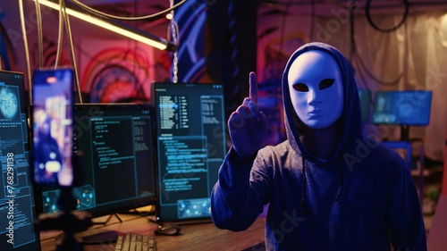 Masked hackers filming video threatening to not stop coordinating DDoS attack on website and send large amounts of traffic from multiple sources to overwhelm it unless their demands are not met