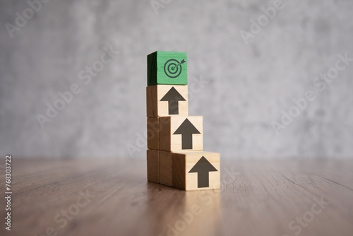 A stack of wooden blocks with arrows pointing upwards and target board. Mission, focus, ladder of success concept.