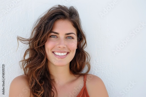A portrait of a radiant woman with long brown hair and green eyes smiling joyfully against a white backdrop