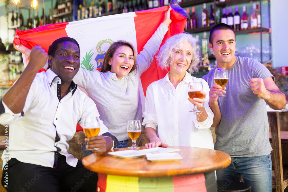Happy sport fans holding flag of Peru, celebrating victory of national team, drinking alcoholic drinks in beer pub