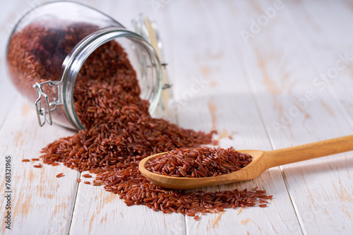 Raw red rice in wooden scoop and in glass storage jar on a white wooden table. photo