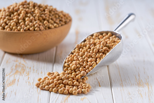 Raw soybeans in a metal scoop on a white wooden table.