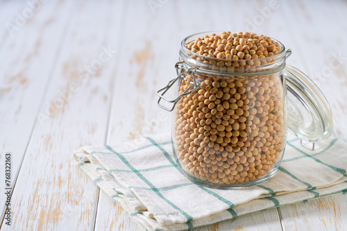 Raw soybeans in glass storage jar on a white wooden table.