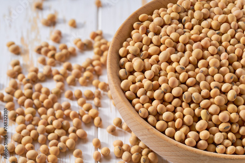 Organic soybeans are scattered out of the wooden bowl on a light table, selective focus.