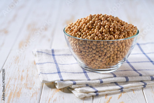 Raw soybeans in a glass plate on a white wooden table.