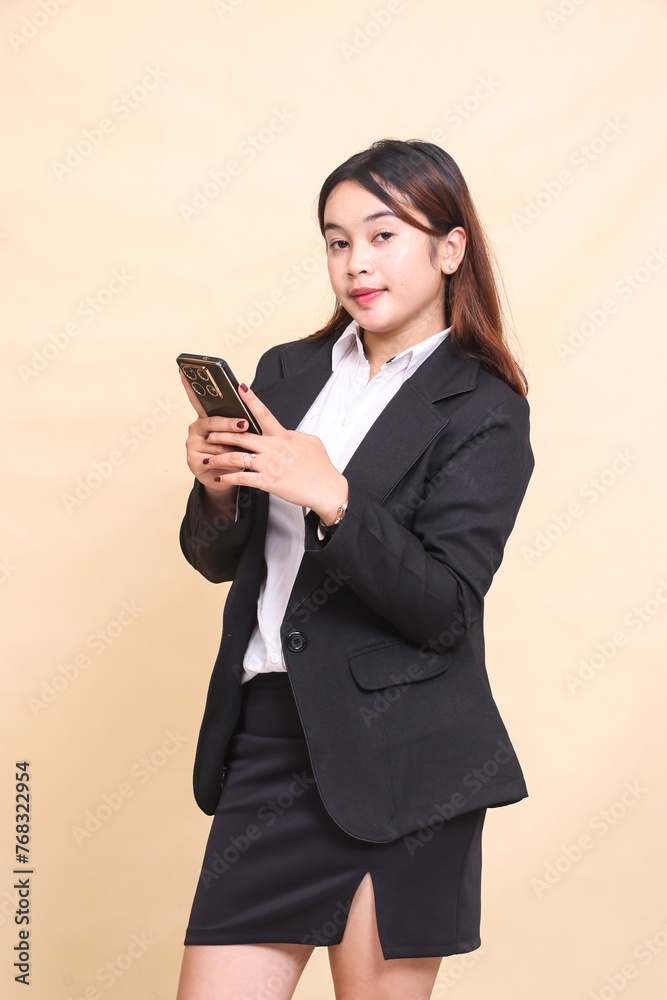Beautiful formal indonesia executive woman in suit elegant standing and holding while operating smartphone gadget chatting with her friend on yellow background for commercial, vacancies and business Beautiful formal indonesia executive woman in suit elegant standing and holding while operating smartphone gadget chatting with her friend on yellow background for commercial, vacancies and business