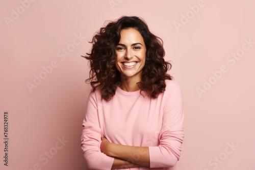 Portrait of a happy young woman standing with arms crossed over pink background