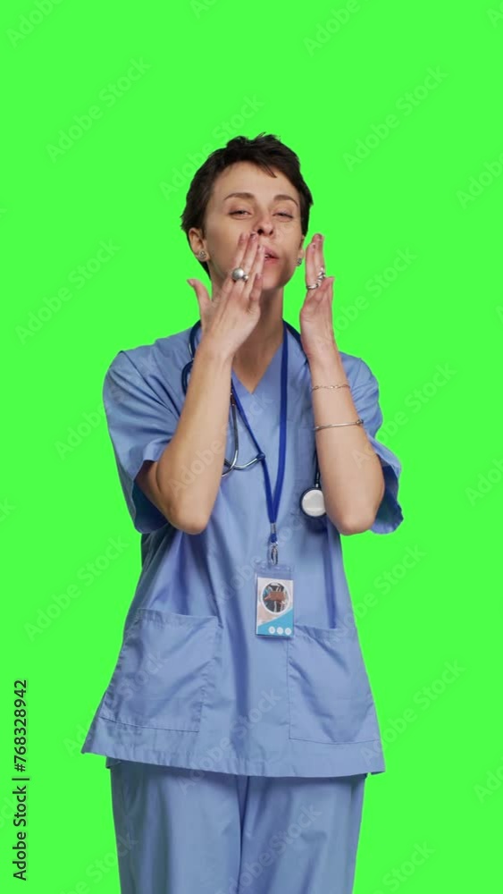 Front view Flirty cute nurse blowing air kisses against greenscreen backdrop, being romantic and expressing sweet feelings. Medical assistant in scrubs doing lovely gesture, expressing true love