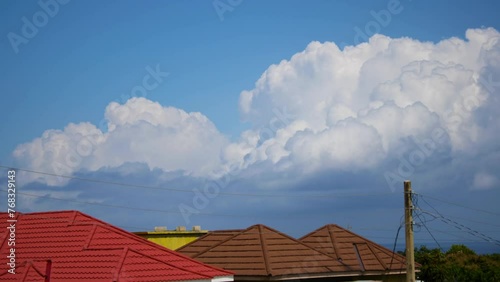 Fluffy white cumulus clouds moving in blue sky above house rooftops time lapse 2