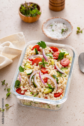 Pearl couscous salad with fresh vegetables and herbs in a meal prep container, healthy lunch or side dish photo