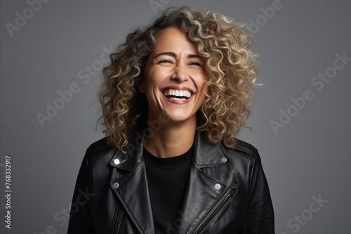 Happy woman with curly hair laughing and looking at camera over grey background