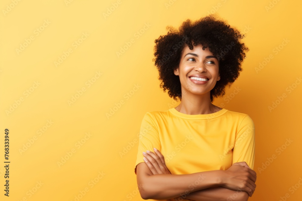 Portrait of a smiling afro american woman with crossed arms looking away over yellow background Portrait of a smiling afro american woman with crossed arms looking away over yellow background
