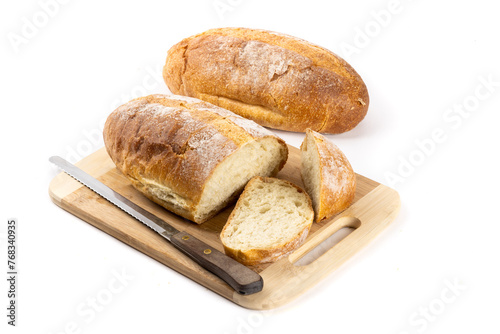 A whole loaf of artisanal crusty bread with slice cut off on a wooden cutting board and another loaf in the background isolated on white