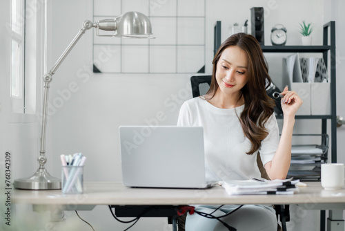 Thoughtful businesswoman at her organized workstation, contemplating while working on a laptop in her bright and modern home office.