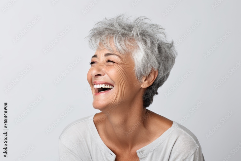 Portrait of a happy senior woman laughing and looking up against grey background