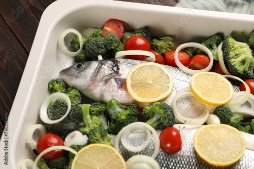 Raw fish with vegetables and lemon in baking dish on table