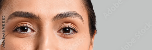 Young woman receiving filler injection in face against grey background