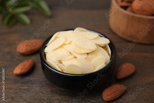 Fresh almond flakes in bowl and nuts on wooden table, closeup