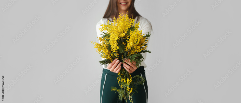 Young woman holding bouquet of beautiful mimosa flowers on light background - obrazy, fototapety, plakaty 