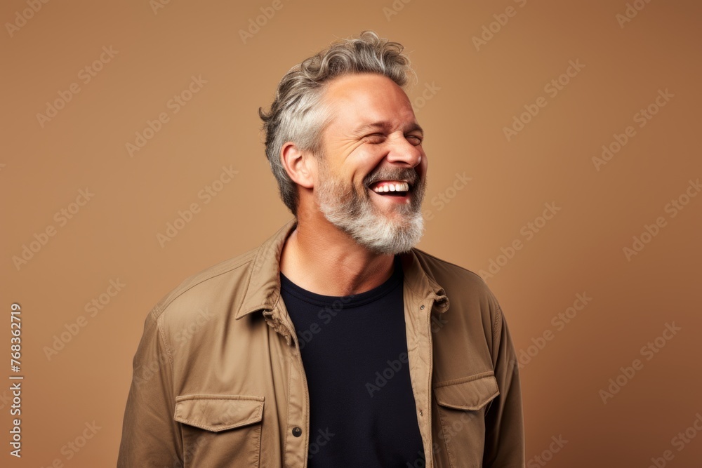 Senior man with grey hair and beard laughing. Studio shot on brown background.