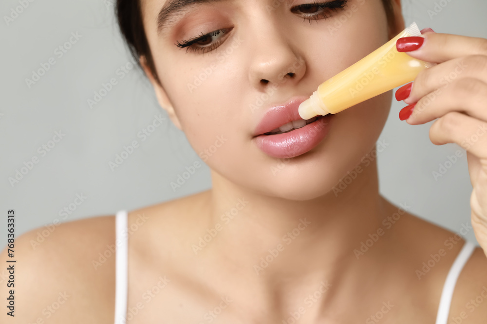 Young woman applying lip balm on grey background, closeup Young woman applying lip balm on grey background, closeup