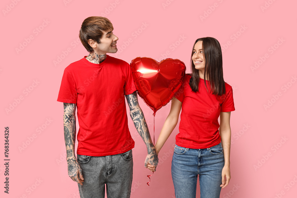Young couple with heart-shaped air balloon holding hands on pink background