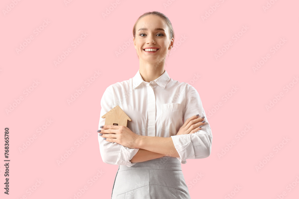Portrait of female real estate agent with wooden house model on pink background Portrait of female real estate agent with wooden house model on pink background