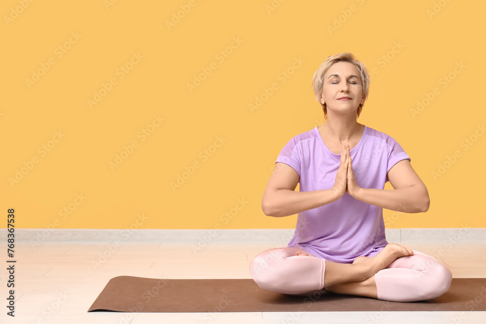 Portrait of meditating mature woman sitting on floor against yellow wall Portrait of meditating mature woman sitting on floor against yellow wall