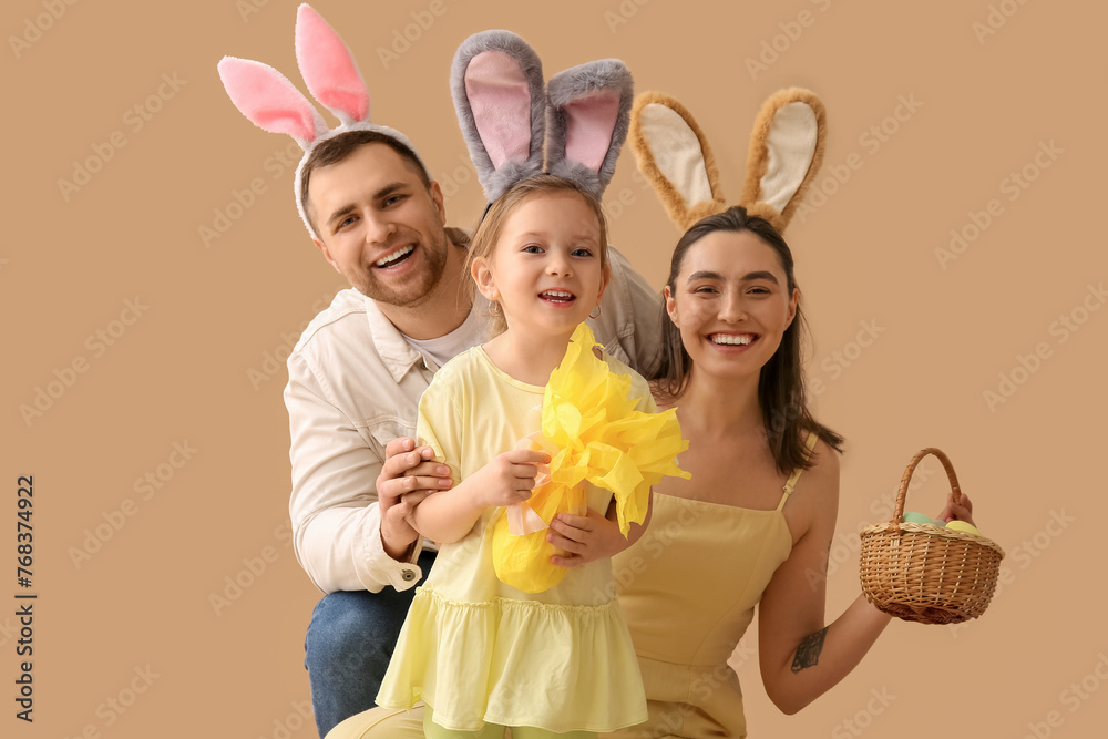 Happy family in bunny ears holding basket with Easter eggs and gift on beige background Happy family in bunny ears holding basket with Easter eggs and gift on beige background