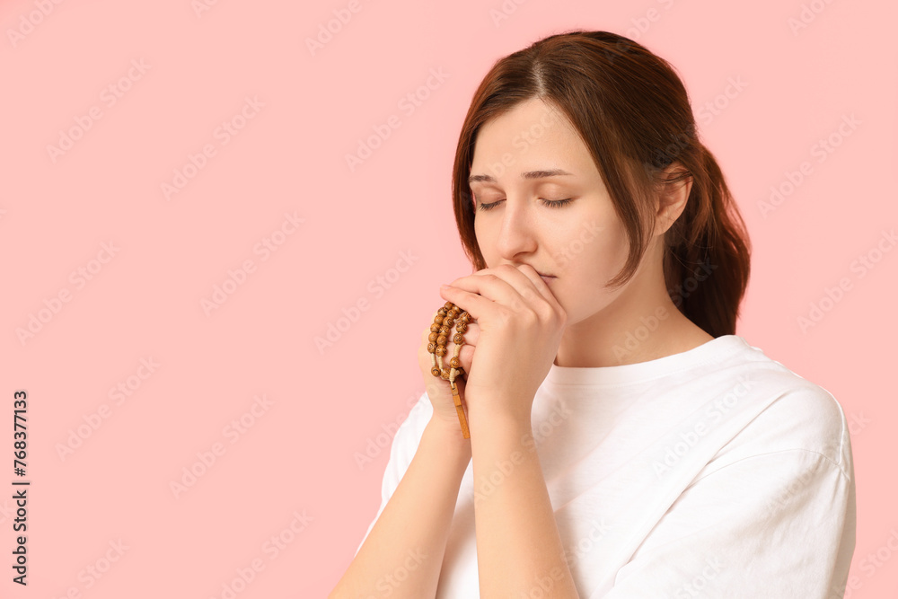 Religious young woman praying on pink background Religious young woman praying on pink background