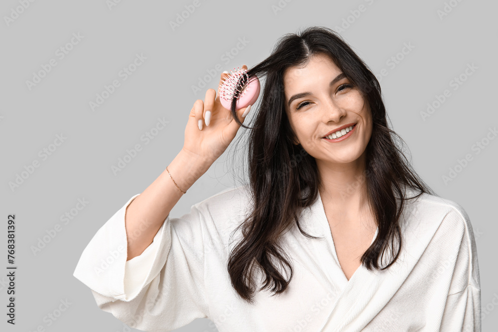 Pretty young woman brushing her hair on grey background Pretty young woman brushing her hair on grey background