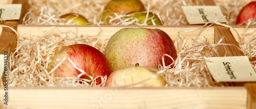 Three apples are in a wooden crate with straw