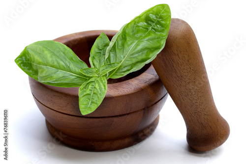 Basil leaves in wooden mortar and pestle on white background.