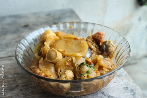 Seblak is a typical Indonesian dish with a savory and spicy taste. cooked with vegetables, sausage, eggs, chicken feet, seafood and processed beef. a bowl of seblak on a wooden table. photo