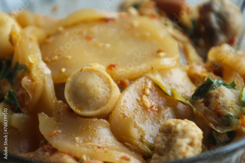 Seblak is a typical Indonesian dish with a savory and spicy taste. cooked with vegetables, sausage, eggs, chicken feet, seafood and processed beef. a bowl of seblak on a wooden table.