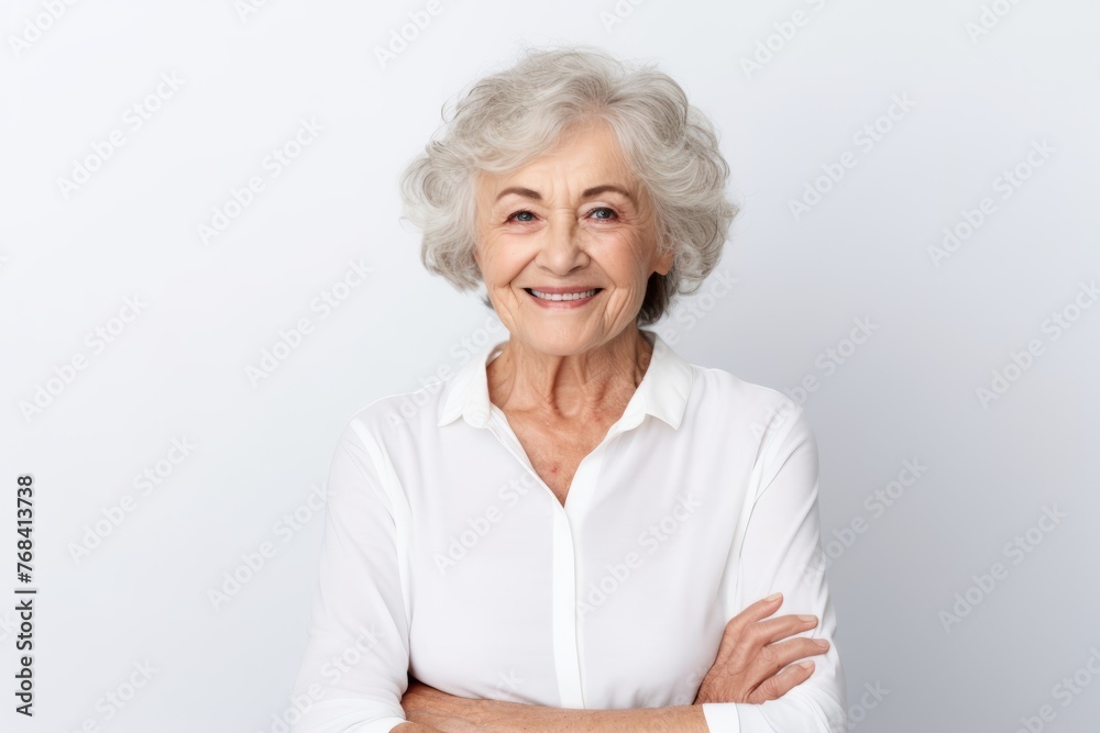 Portrait of a happy senior woman standing with arms crossed against grey background Portrait of a happy senior woman standing with arms crossed against grey background