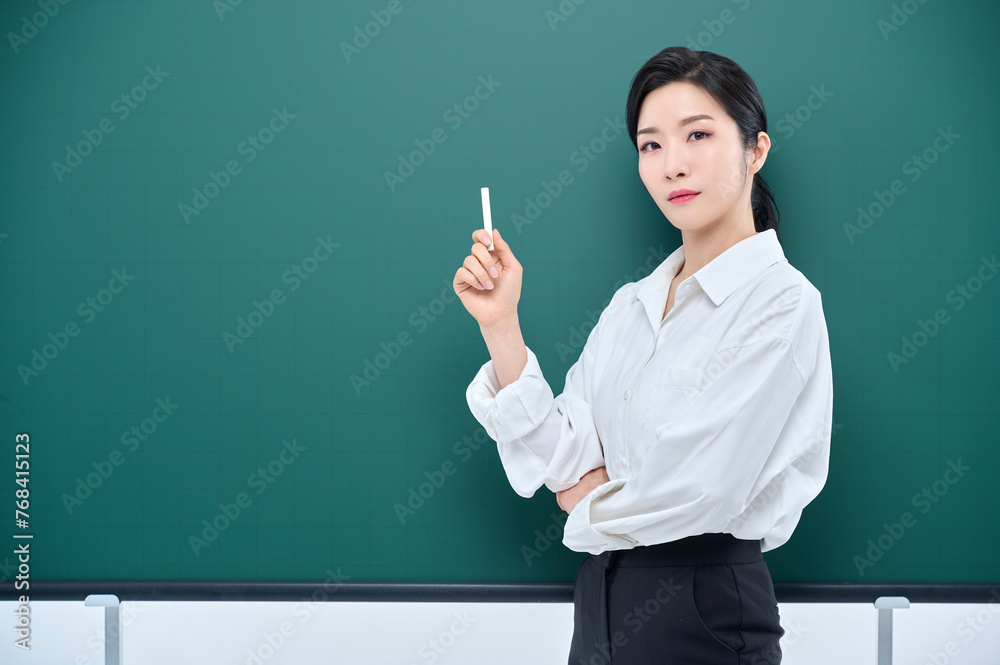 Wearing white heating, a beautiful Asian female teacher is holding a chalk in front of a green chalkboard and giving an Internet lecture with a confident expression and pose. Wearing white heating, a beautiful Asian female teacher is holding a chalk in front of a green chalkboard and giving an Internet lecture with a confident expression and pose.
