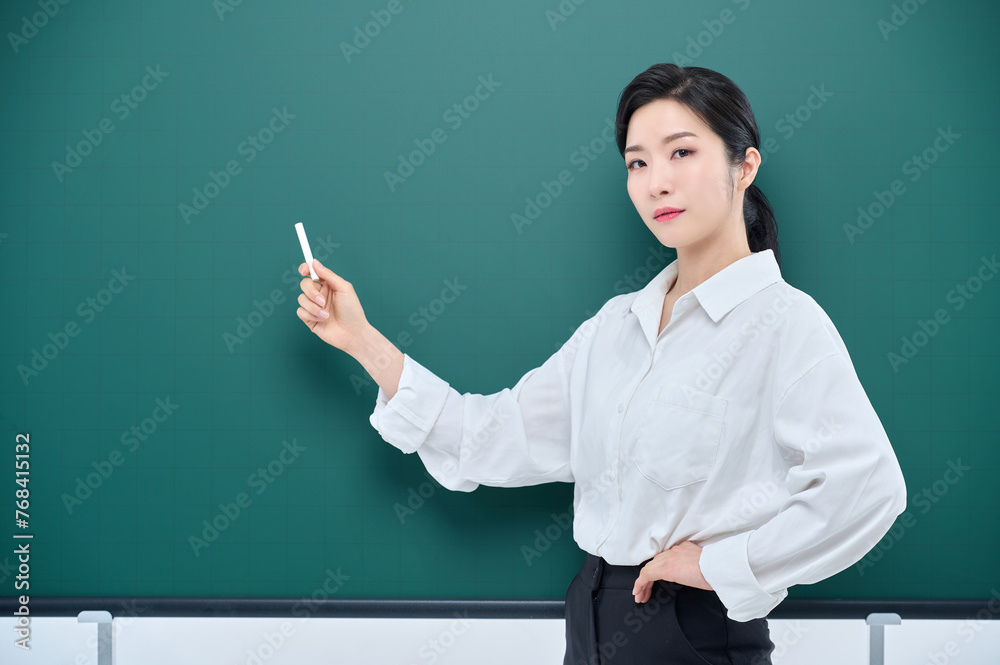 Wearing white heating, a beautiful Asian female teacher is holding a chalk in front of a green chalkboard and giving an Internet lecture with a confident expression and pose. Wearing white heating, a beautiful Asian female teacher is holding a chalk in front of a green chalkboard and giving an Internet lecture with a confident expression and pose.